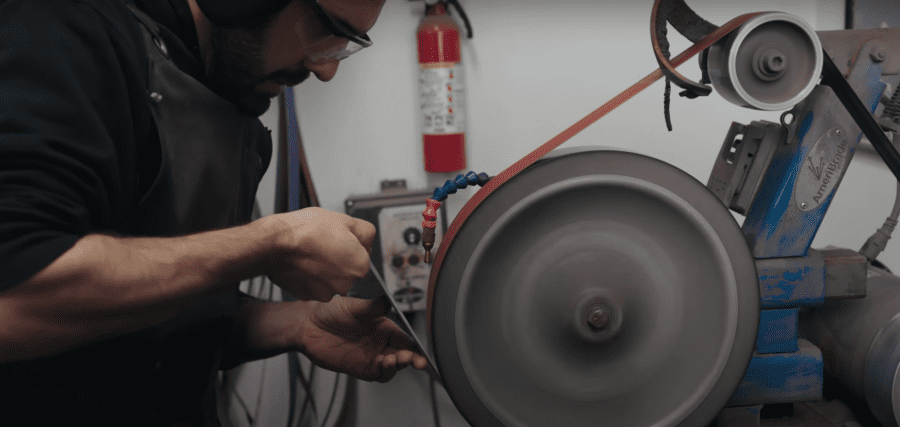Knifemaker at a grinding machine, working on a blade.