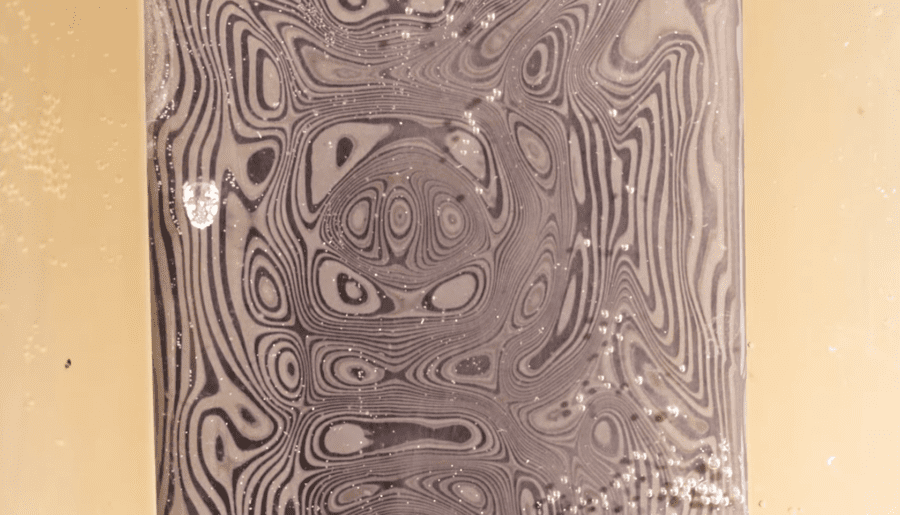 Damascus steel billet submerged in etching acid, bubbling and revealing the pattern