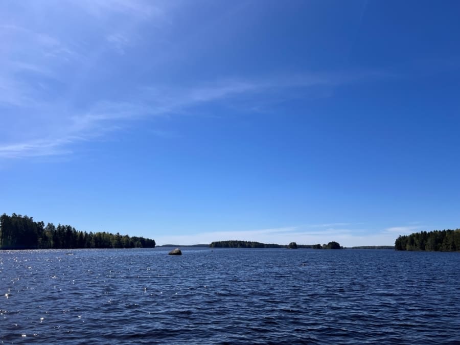 Bright blue sky on top of dark blue lake water, small forested islands in the distance